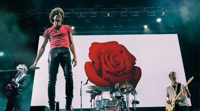 Band The Kooks performing on stage, with an image of a rose against a white background as the stage screen